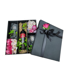 Box with orchids, roses, tropical leaves, wine and glasses